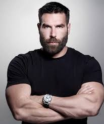 Dan Bilzerian in a black shirt and wristwatch with a grey background